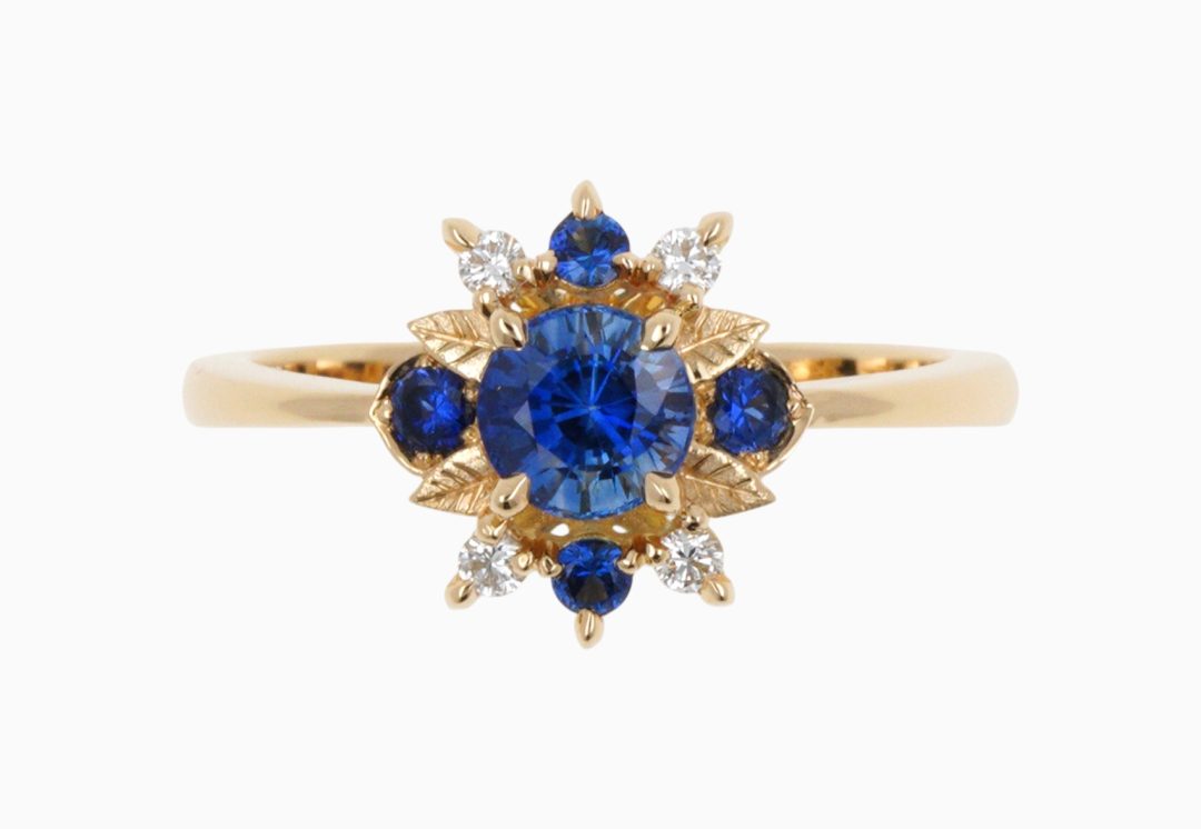 Bague en or jaune sertie d'un saphir bleu et diamants avec motif feuille sculptée.