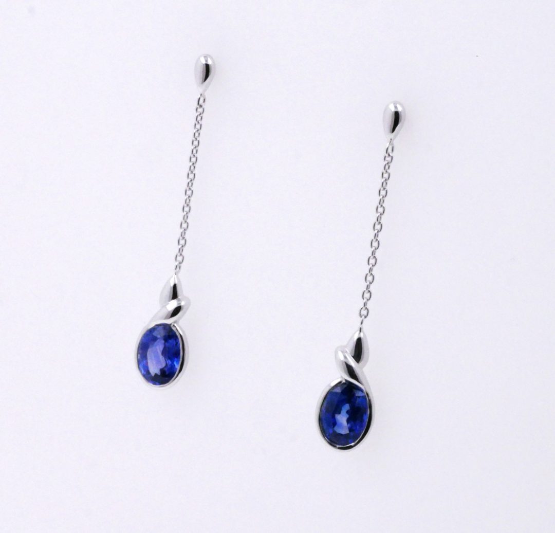 Boucles d'oreilles pendantes fines en or blanc avec saphir bleu serti clos.